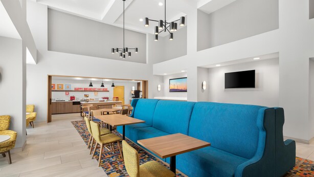 A modern hotel lobby with a blue sofa, wooden tables, yellow chairs, a kitchen area, and a flat-screen TV. - Hampton Inn & Suites New Castle (New Castle)