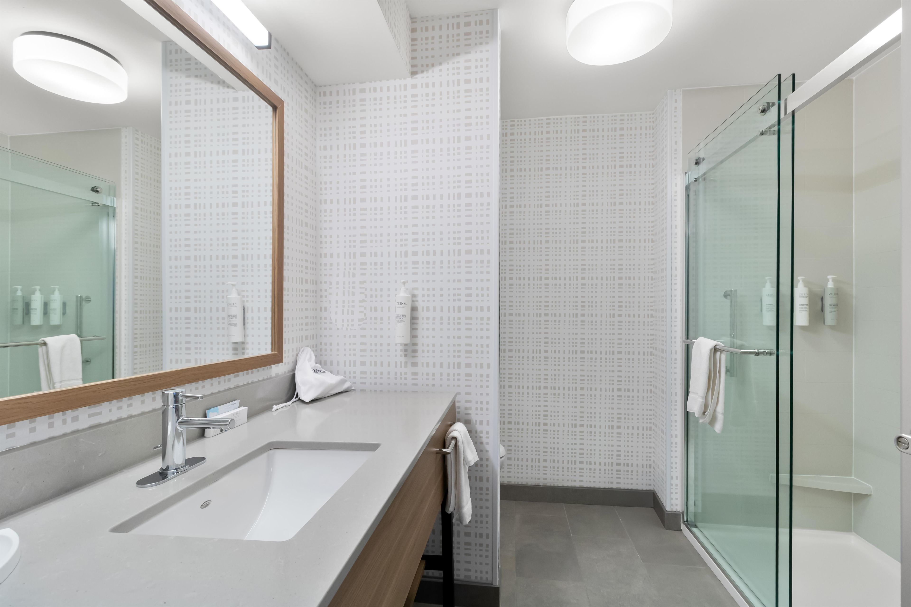 A modern bathroom with a large mirror, a sink, and a glass shower enclosure.