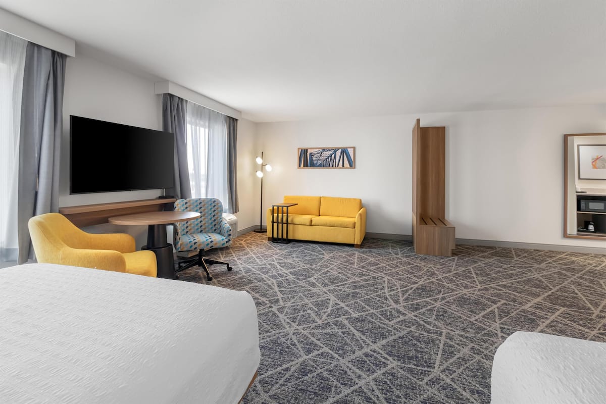 A hotel room with a bed, a sofa, a TV, a desk, and a patterned carpet.
