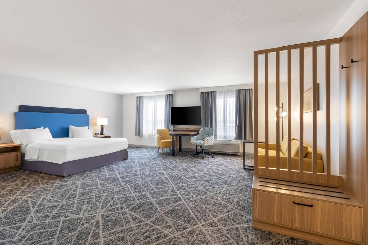 A hotel room with a bed, a desk, a chair, a TV, and a wooden partition.