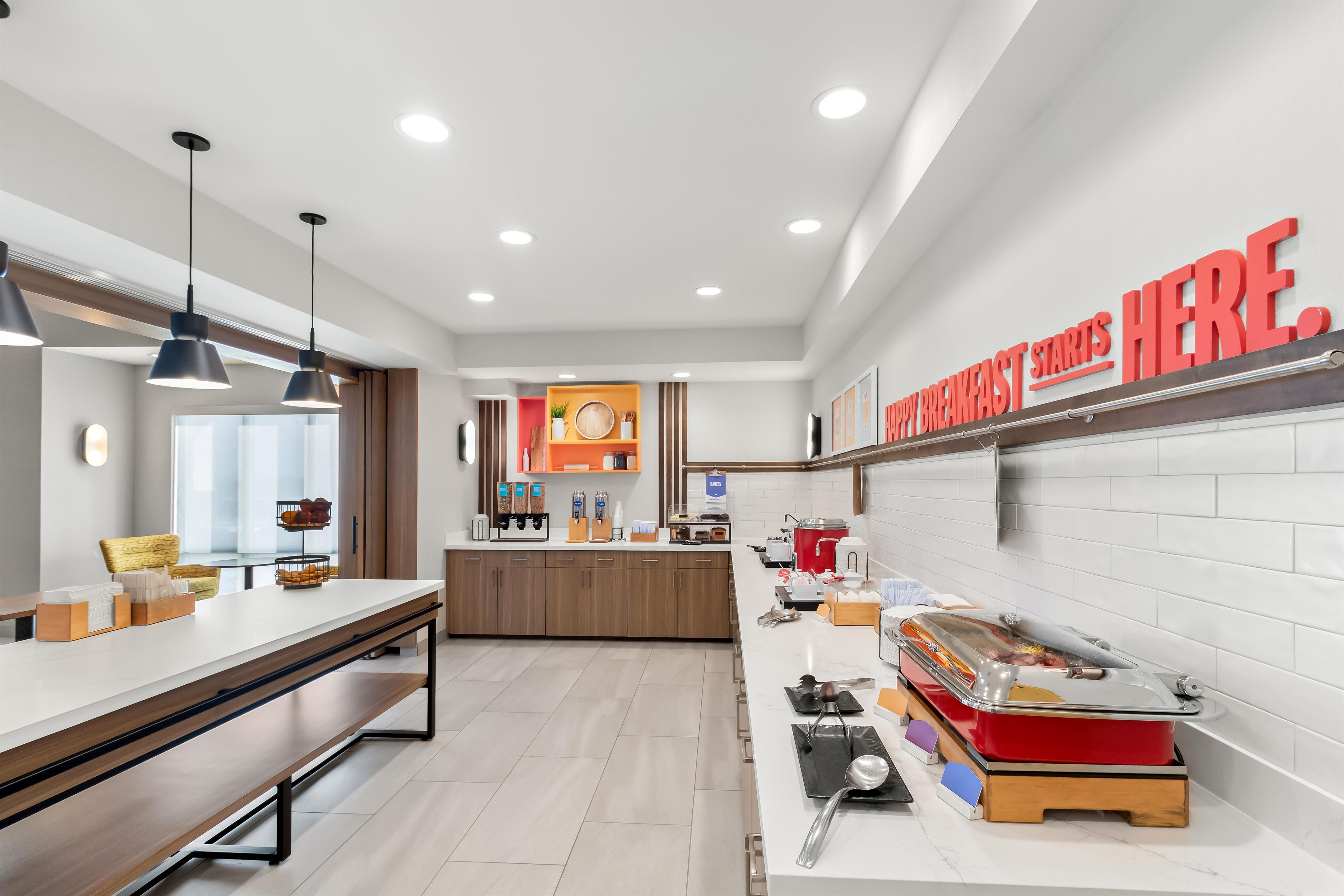 A modern kitchen with a breakfast bar, wooden cabinets, and a sign that reads 'HAPPY BREAKFAST STARTS HERE.'
