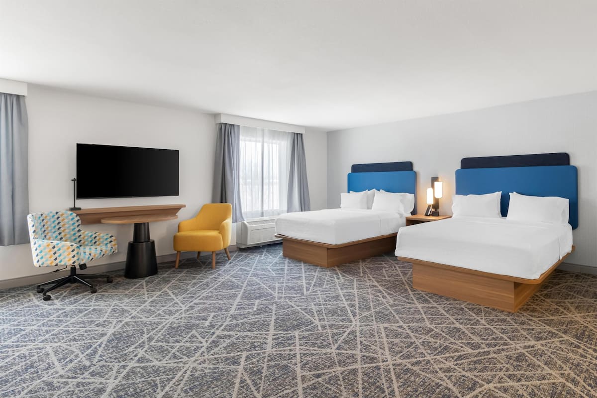 A hotel room with two beds, a TV, a desk, a chair, and a patterned carpet.