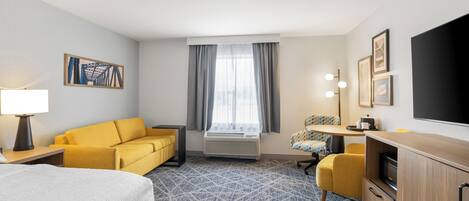 A hotel room with a bed, a yellow sofa, a desk with a chair, and a TV.