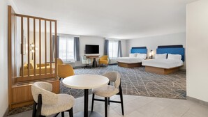 A hotel room with a bed, two bedside tables, a TV, a sofa, a dining table with chairs, and a decorative partition. - Hampton Inn & Suites New Castle (New Castle)