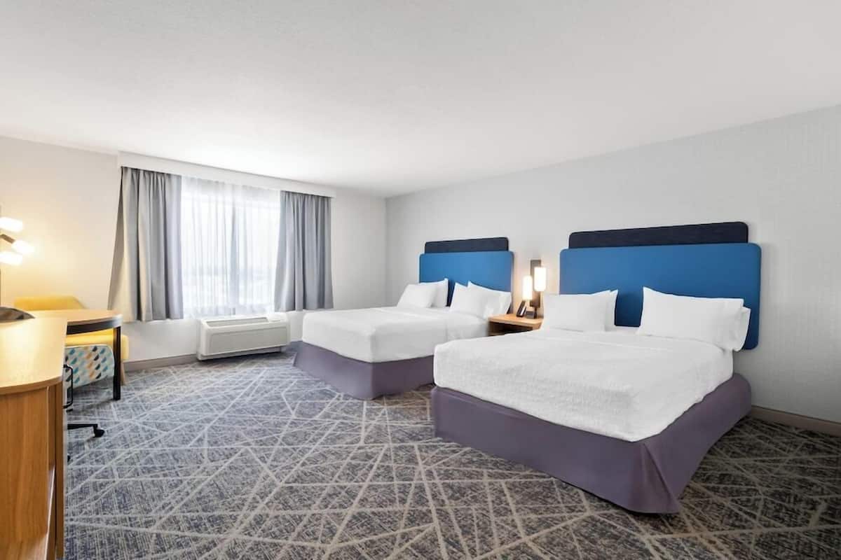 Una habitación de hotel con dos camas, un escritorio y una ventana con cortinas.