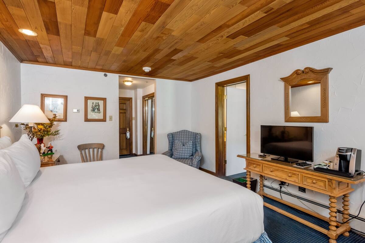 A hotel room with a large bed, a wooden desk with a TV, a chair, and a mirror.