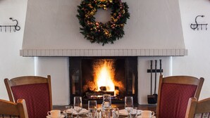 Un comedor con chimenea, una mesa preparada para cuatro personas y un adorno festivo sobre el fuego.