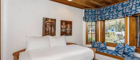 Un dormitorio con una cama de madera, un ventanal con vistas a un bosque y dos cuadros colgados en la pared.
