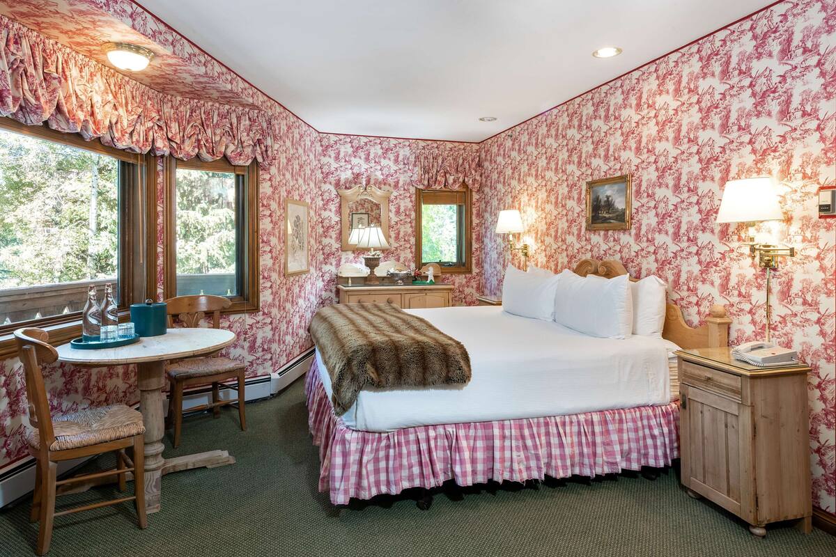 A bedroom with a bed, a desk, a chair, a nightstand, and a window.