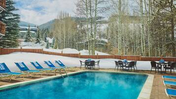 A swimming pool with lounge chairs and tables, surrounded by a wooden fence and snow-covered ground.