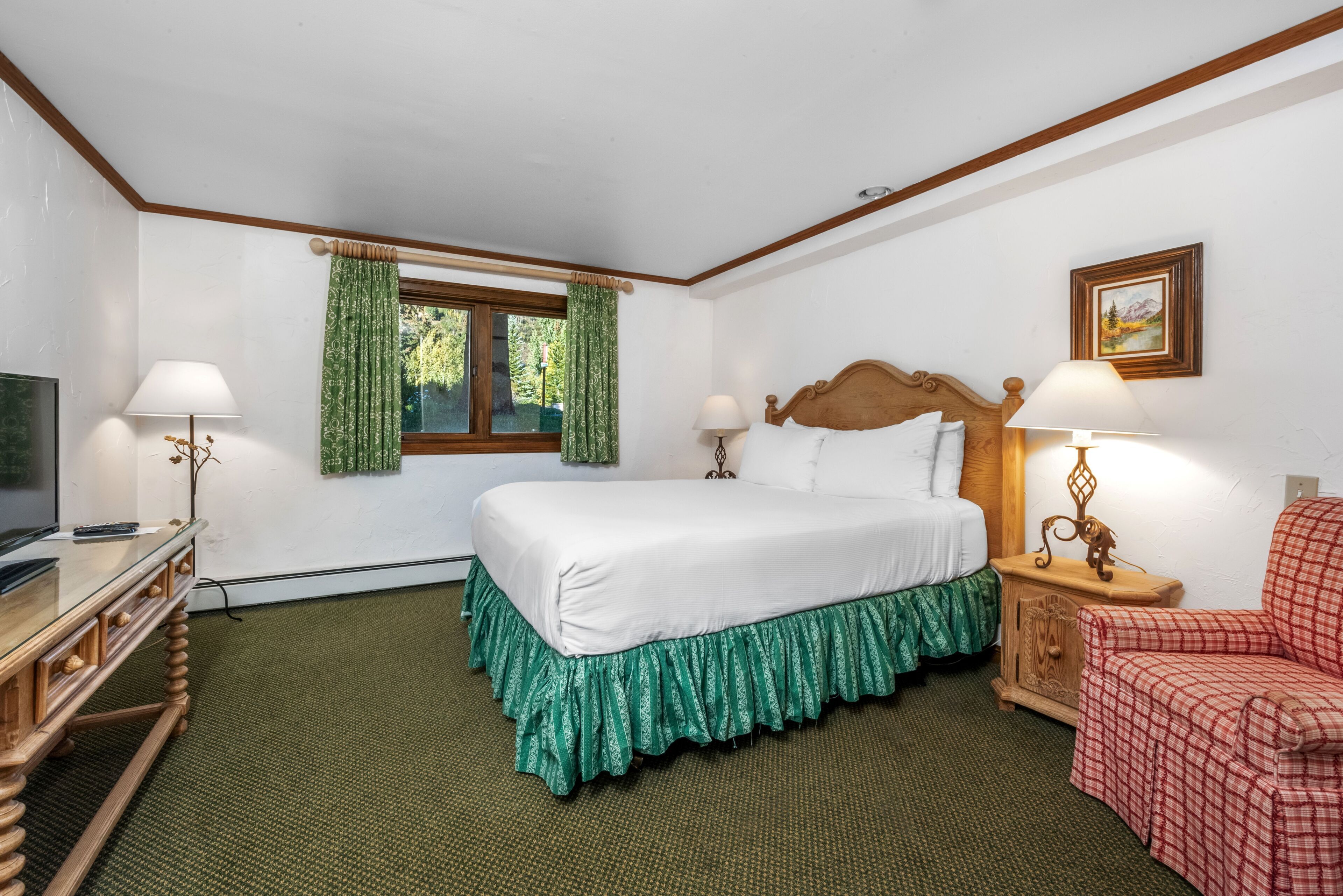 Habitación de hotel con cama, dos mesitas de noche con lámparas, una silla, un televisor y una ventana con cortinas.