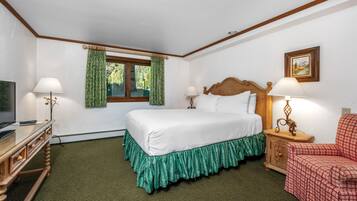 Habitación de hotel con cama, dos mesitas de noche con lámparas, una silla, un televisor y una ventana con cortinas.