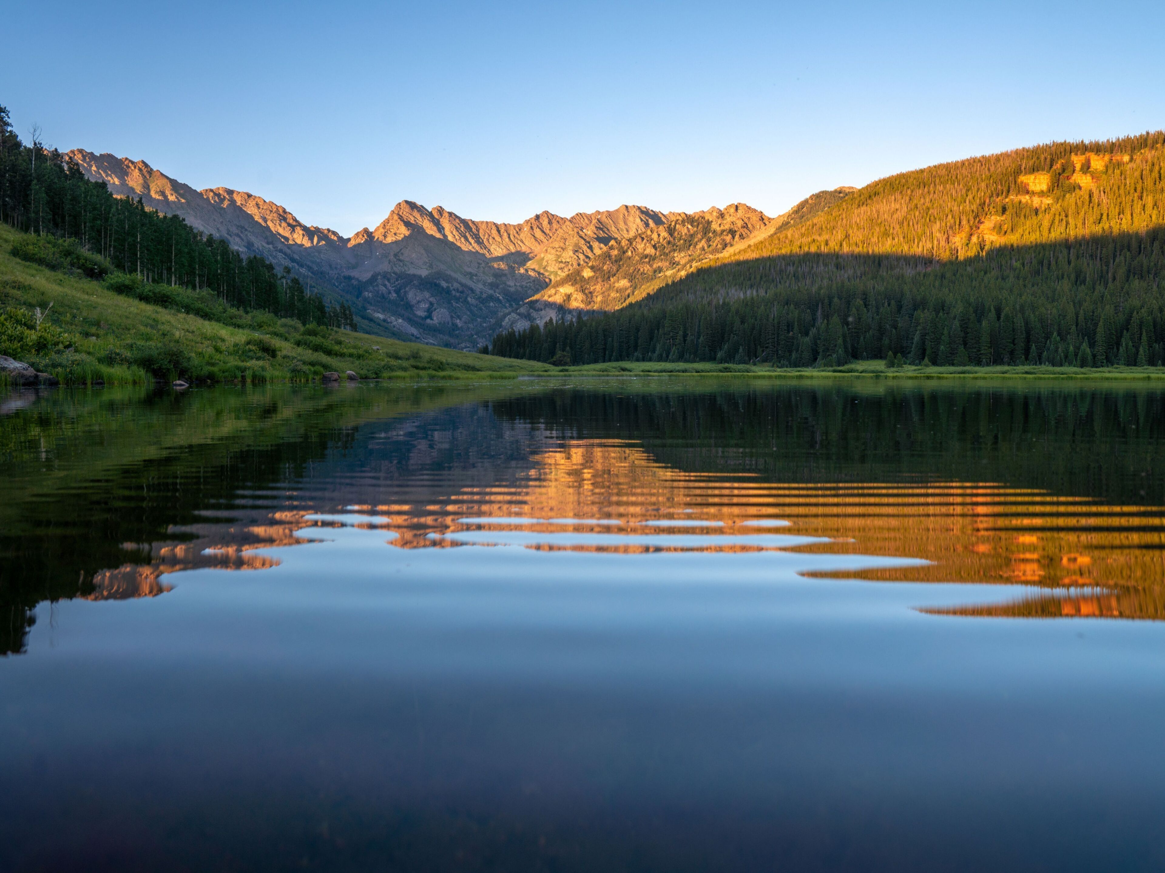 A calm lake reflecting mountains and trees.