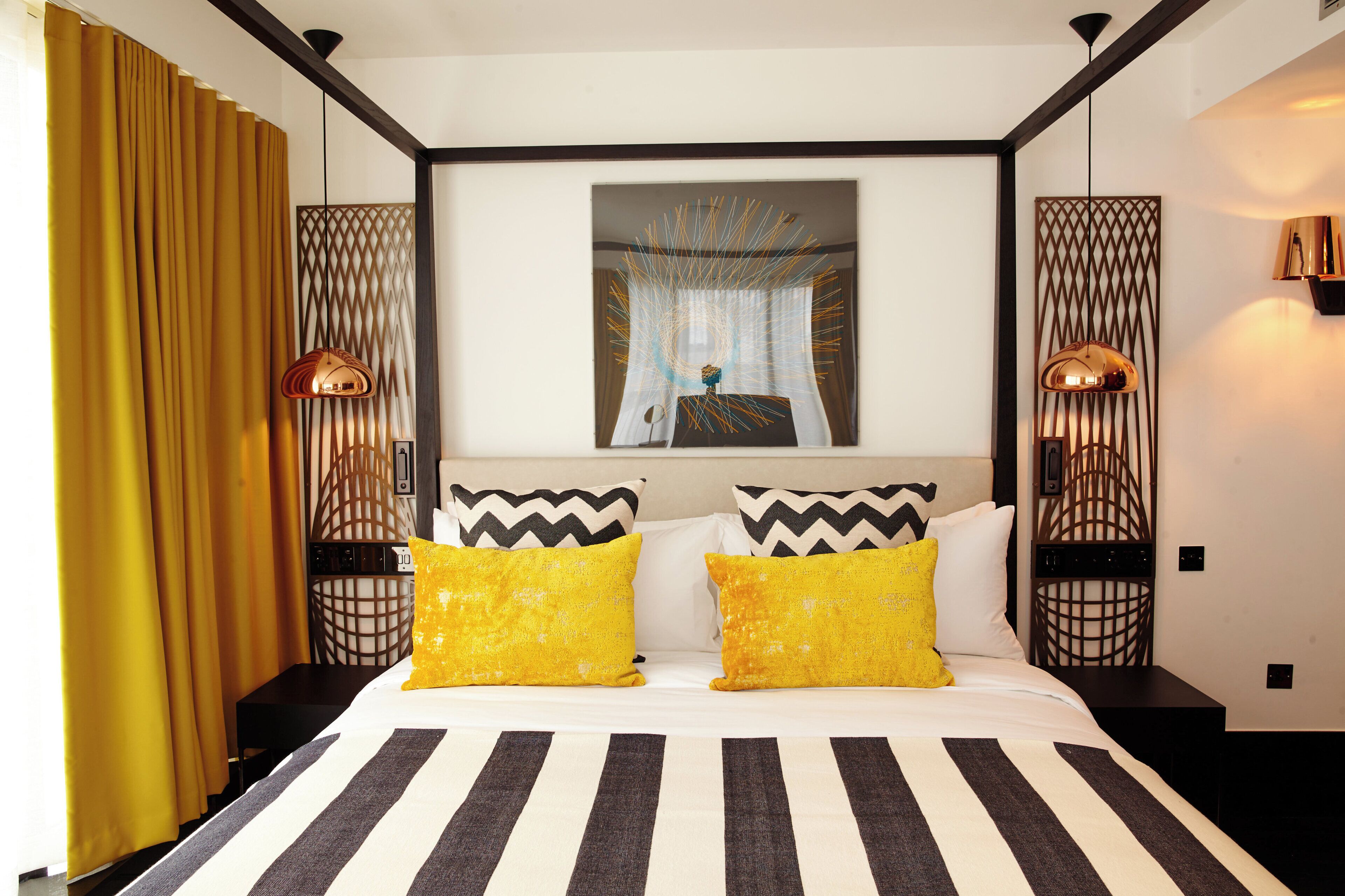 Quarto de hotel com cama, cortinas, um quadro e duas luminárias.