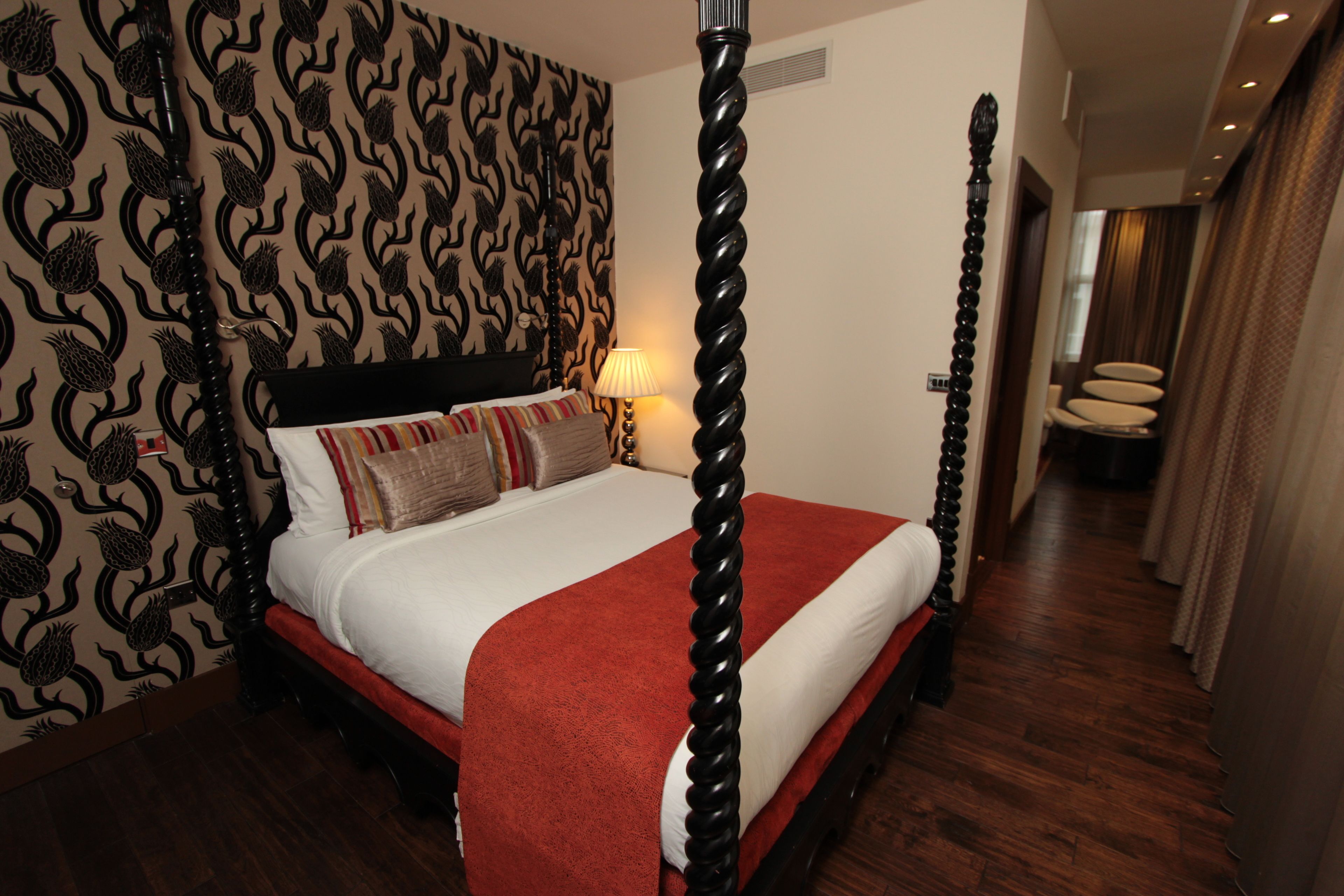 Ein Himmelbett mit roter Bettdecke, Wandpapier mit Muster und Holzboden.