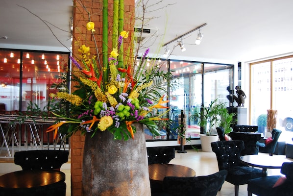 Un espacio interior moderno con un gran arreglo floral, sillas tapizadas en negro y un amplio ventanal con vistas al exterior.