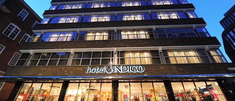 A multi-story hotel with a prominent sign reading 'hotel INDIGO' and large windows displaying interior decor.
