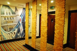 Un couloir d’hôtel avec un mur en briques, une moquette rayée aux couleurs vives et une fresque représentant un pont.
