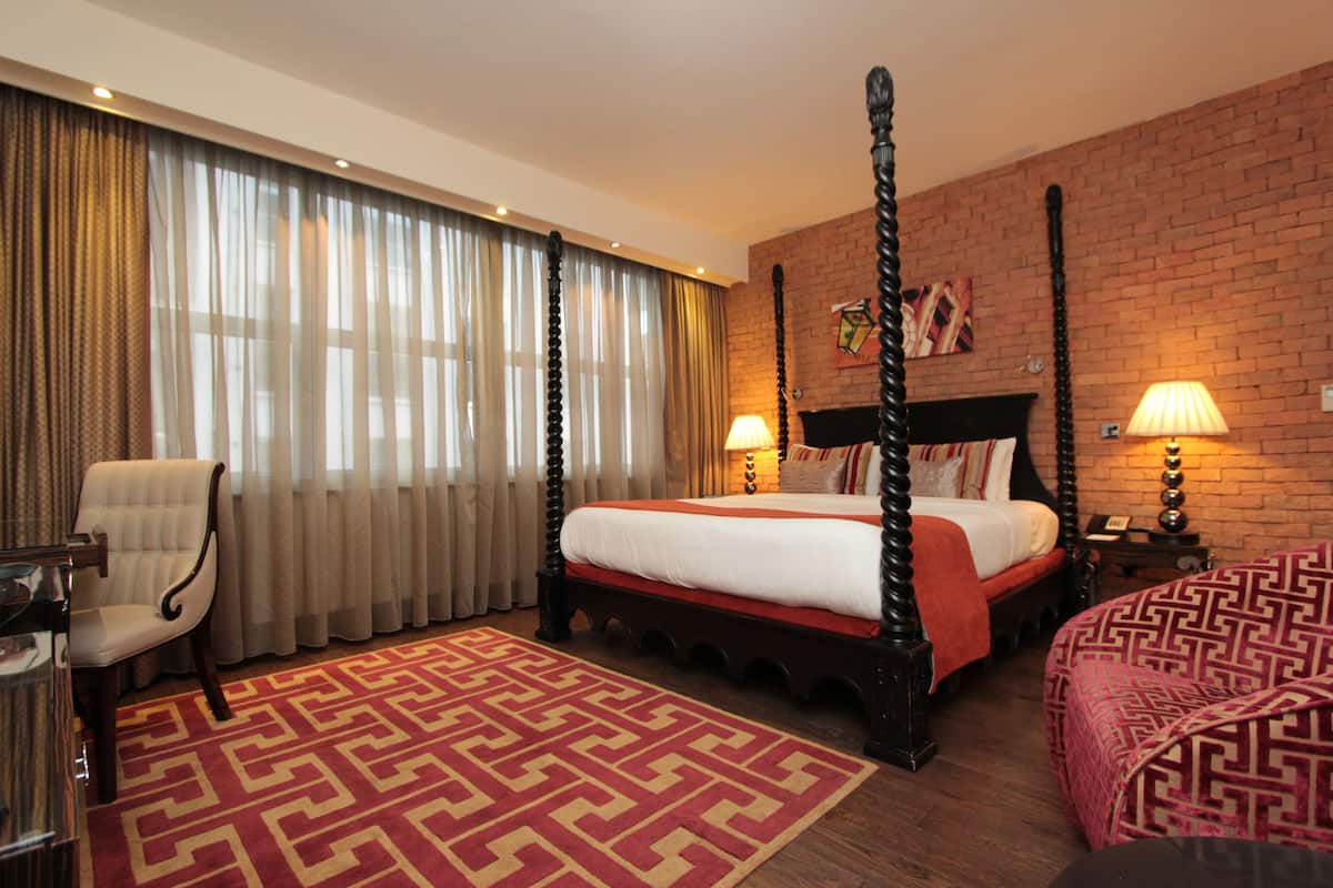 Een hemelbed met een rood-witte spreideken, een tapijt met een rood patroon, een houten stoel en een bakstenen muur.