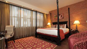 A four-poster bed with a red and white bedspread, a red patterned rug, a wooden chair, and a brick wall.