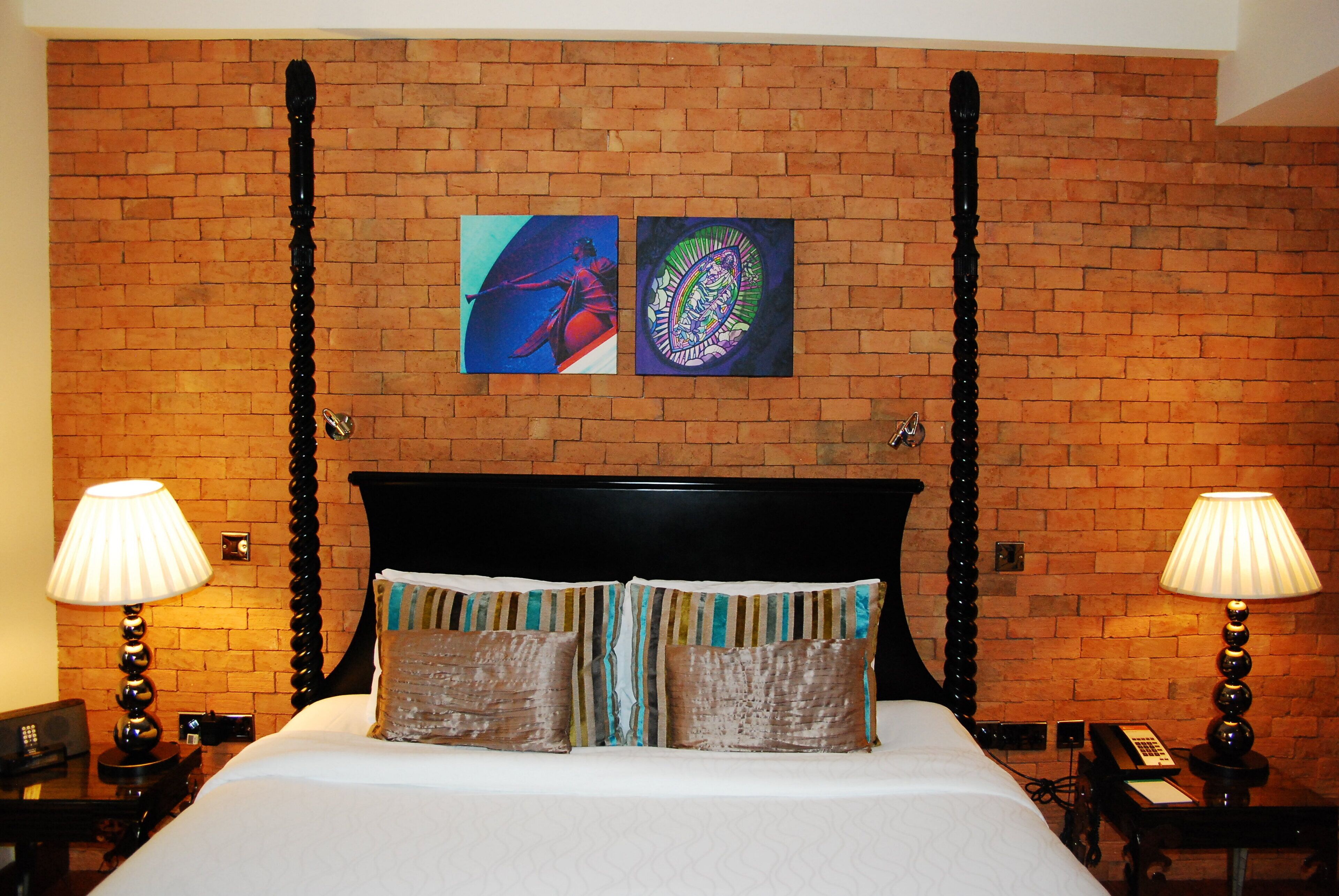 A hotel room with a brick wall, a bed with striped pillows, and two bedside lamps.
