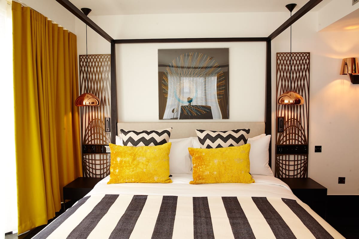 Een hotelkamer met een groot bed, twee nachtkastjes, een wandlamp en een raam met gordijnen.