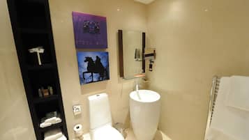 A modern bathroom with a large white sink, a toilet, a glass shelf with toiletries, and a mirror.