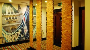 Un couloir orné d’une fresque représentant un bâtiment, avec un escalier mécanique, des colonnes en briques et un tapis à rayures.