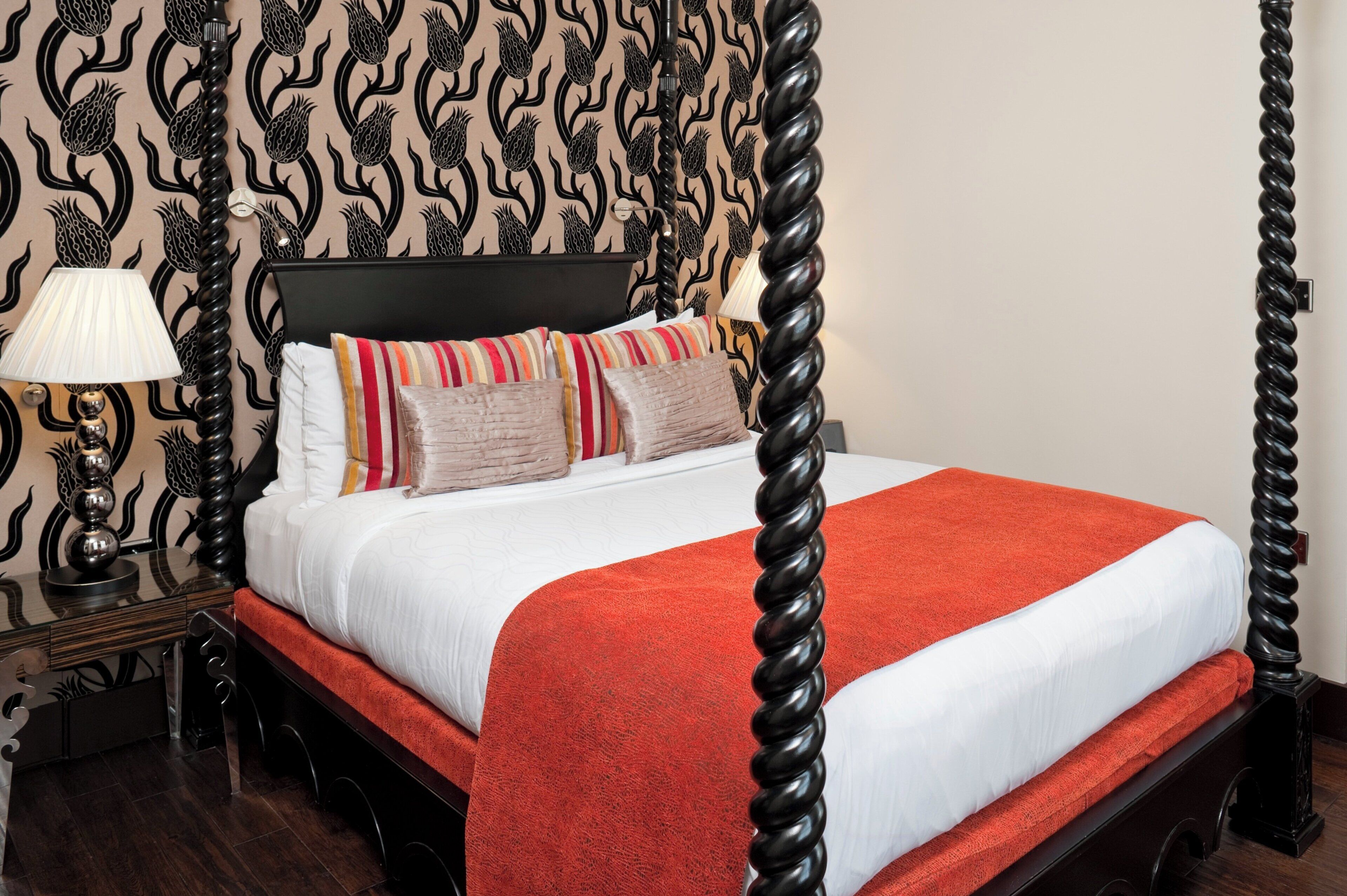 Un lit à baldaquin avec une couvre-lit rouge et de nombreux coussins, une tête de lit noire et un papier peint à motifs.