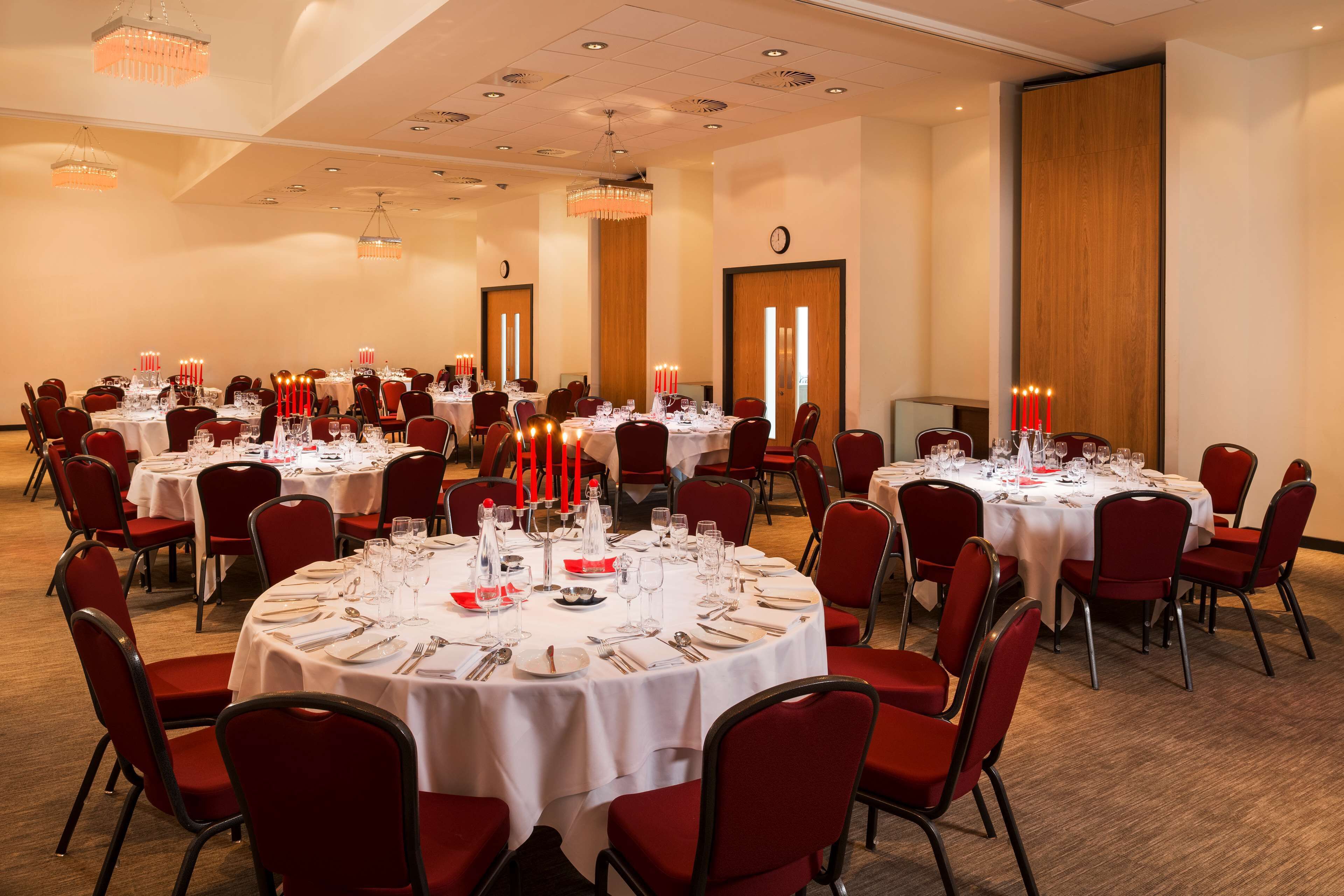 A banquet hall with round tables set for dining, red chairs, and chandeliers.