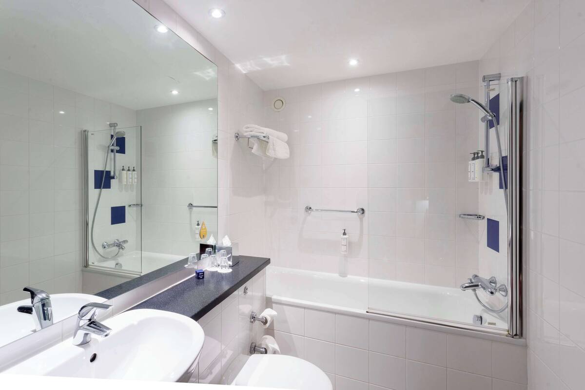 Un baño moderno con ducha de vidrio, bañera y un espejo grande sobre el lavabo.