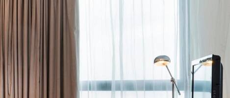 A hotel room with a bed, a desk with a computer, a chair, and a window with curtains.