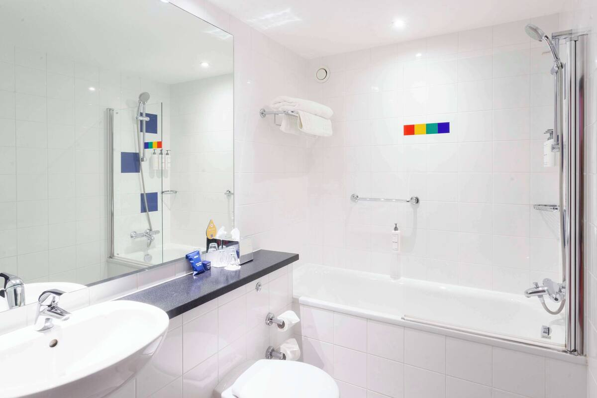 Un baño moderno con un espejo grande, dos lavamanos, una bañera y una ducha.