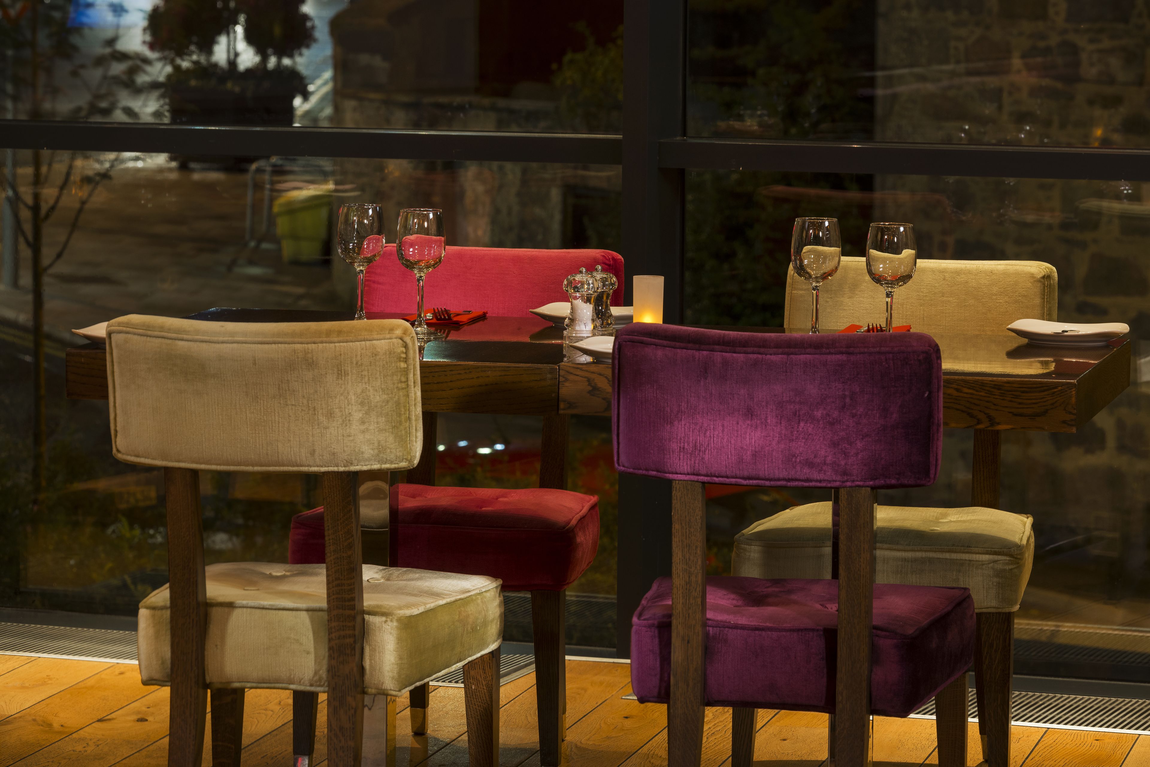 A dining area with cushioned chairs and a table set for two, featuring wine glasses and a candle.