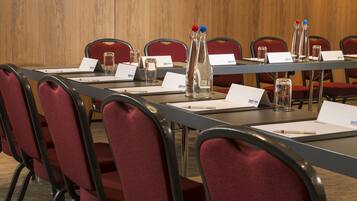 Un salón de conferencias con una larga mesa, sillas rojas, tarjetas de identificación y botellas de agua.