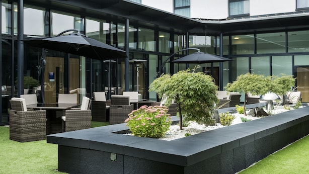 A modern outdoor seating area with wicker furniture and umbrellas, surrounded by greenery and a stone planter. - Park Inn by Radisson Aberdeen (Aberdeen)
