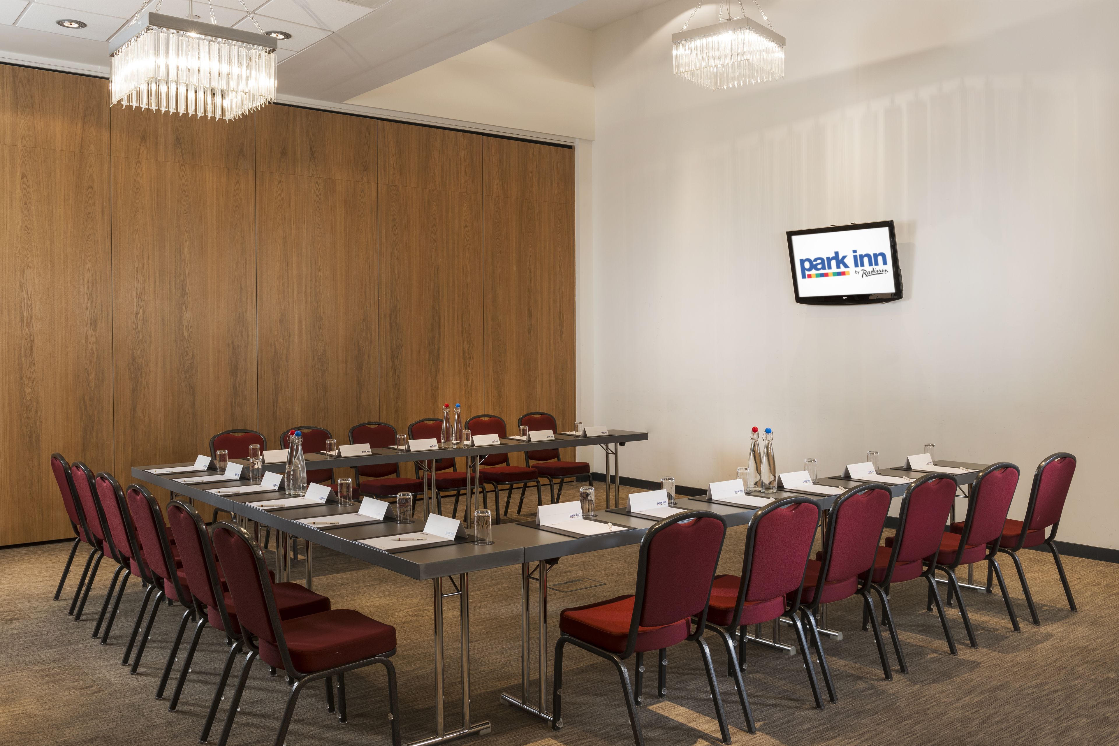 A conference room with a long table, red chairs, nameplates, and a 'Park Inn' sign on the wall.