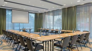 A conference room with long tables, chairs, and a projector screen.