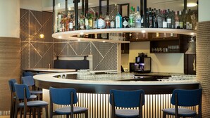 Un área de bar con mostrador curvo, diversas opciones de asientos y una variedad de botellas y copas a la vista.