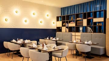 A restaurant with tables set for dining, a bookshelf, and a blue curtain backdrop.