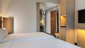 Habitación de hotel con dos camas, un armario de madera, un televisor y un espejo.