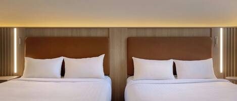 A hotel room with two beds, each with white bedding and a wooden headboard.