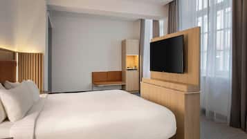 Et moderne hotelværelse med en stor seng, et fladskærms-tv monteret på et træskab, et siddeområde med en sofa og et vindue med gardiner.