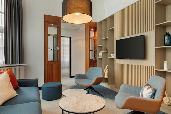 A modern living room with a sofa, two armchairs, a coffee table, a TV, and built-in shelving. - Courtyard by Marriott Bremen (Bremen)