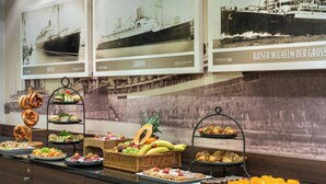 Un bufé con diferentes opciones de comida y tres fotografías enmarcadas de barcos históricos en la pared.