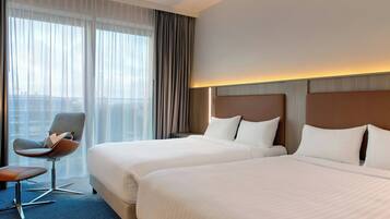 Habitación de hotel con dos camas, una silla y vistas a la ciudad.