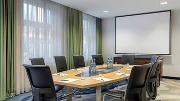 Una sala de conferències amb una taula gran, cadires, ampolles d'aigua i una pantalla de projector.