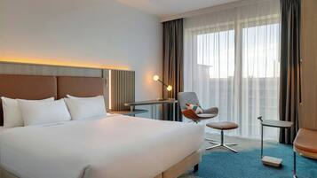Une chambre d’hôtel avec un grand lit, un bureau, une chaise et une vue sur la ville par la fenêtre.