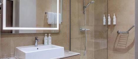 A modern bathroom with a white sink, mirror, and glass shower enclosure.