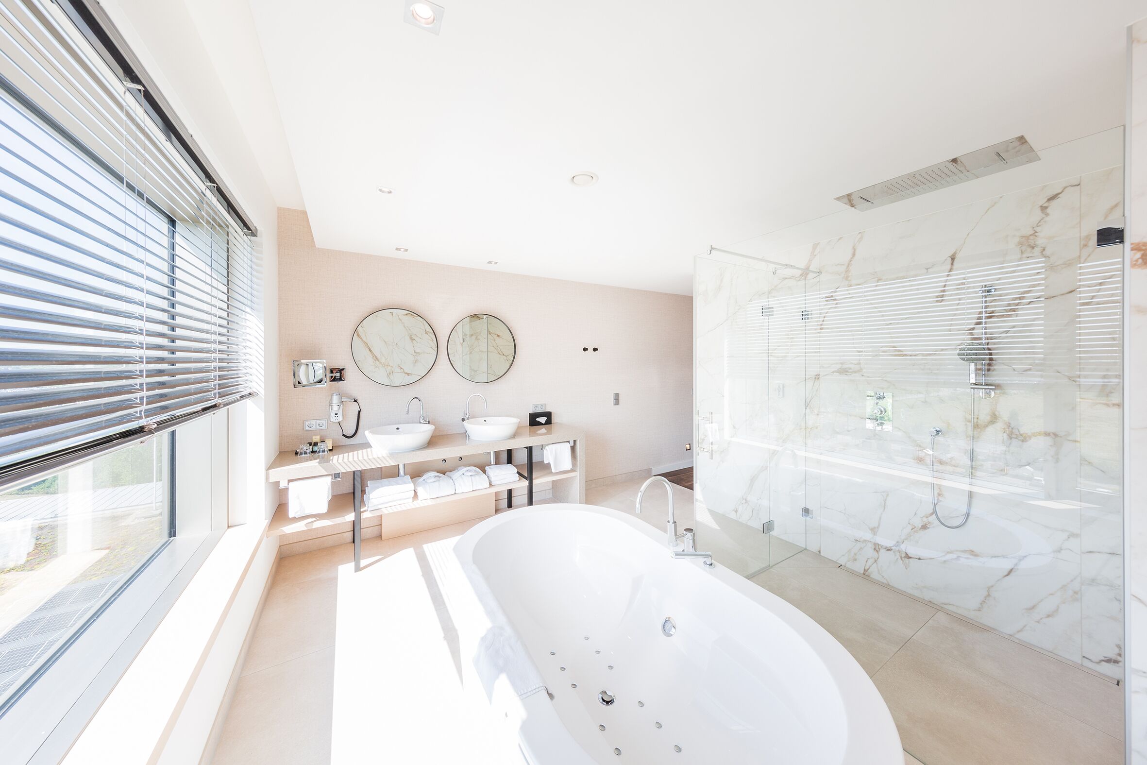 Ein modernes Badezimmer mit einer freistehenden Badewanne, einer in Glaswänden eingeschlossenen Dusche und einem Waschtisch mit Waschbecken und Spiegel.